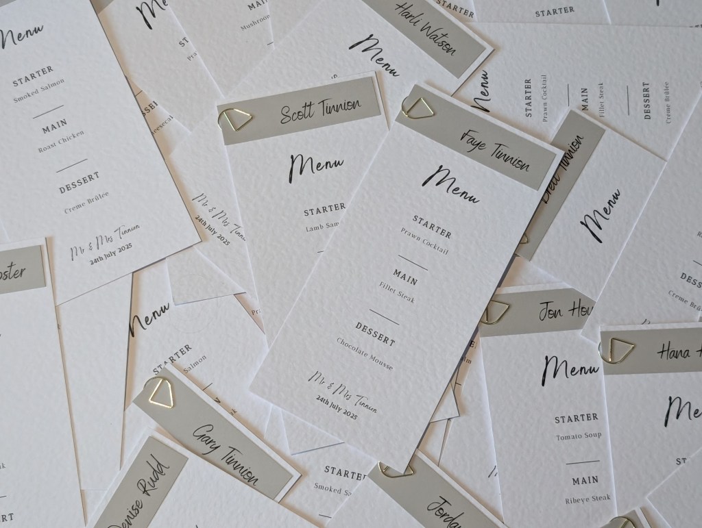 Various wedding menu place cards with personalised grey place names fastened with a gold clip