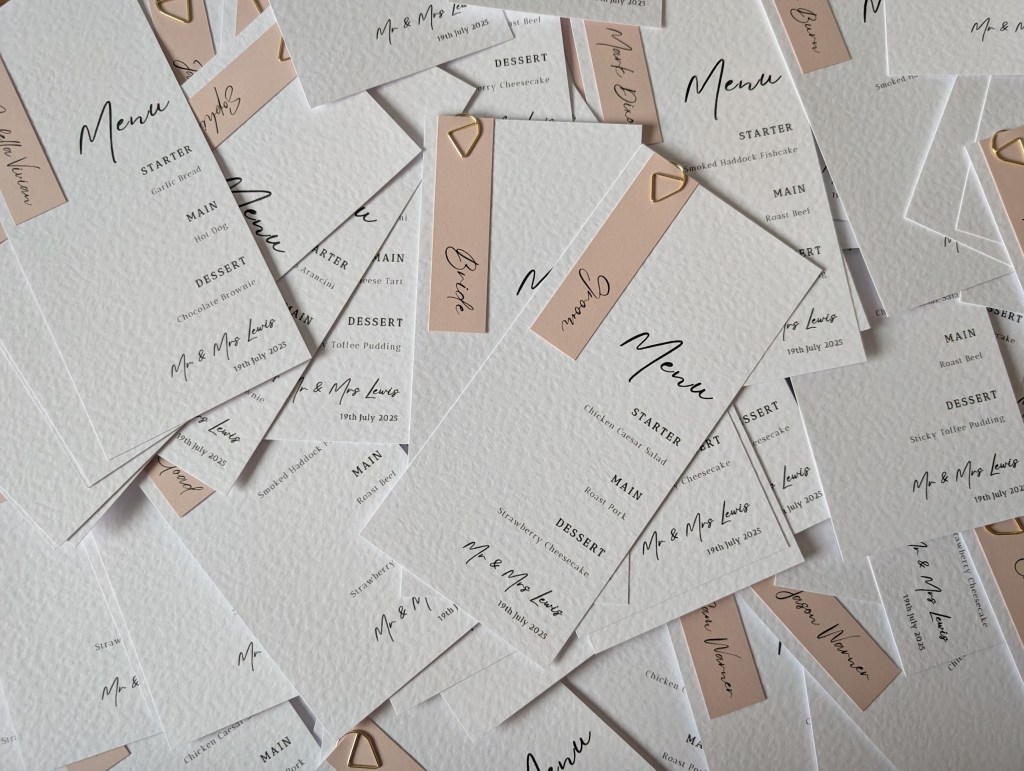 Various wedding menu place cards with personalised dusky pink place names fastened with a gold clip