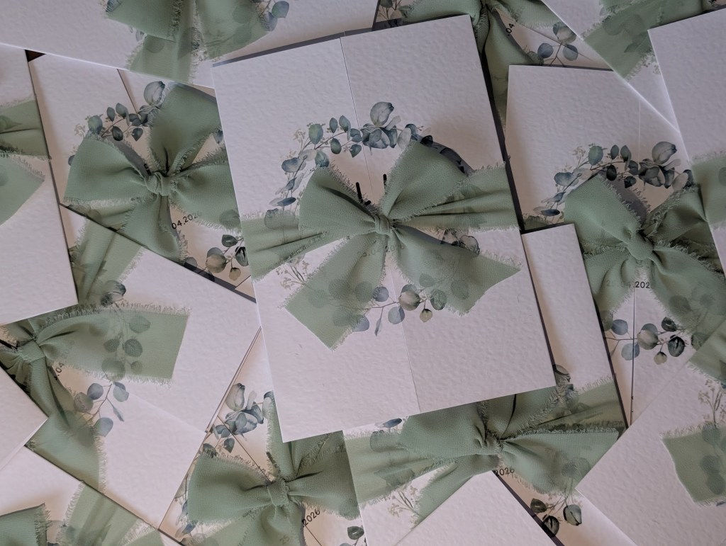 Sage Green Eucalyptus gatefold wedding invitations bound by sage green chiffon bow layered on top of each other